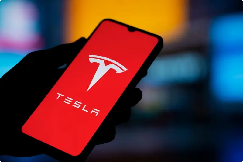 Smartphone met Tesla-logo op het scherm, passend bij Big Tech in de schijnwerpers terwijl beleggers adem inhouden.