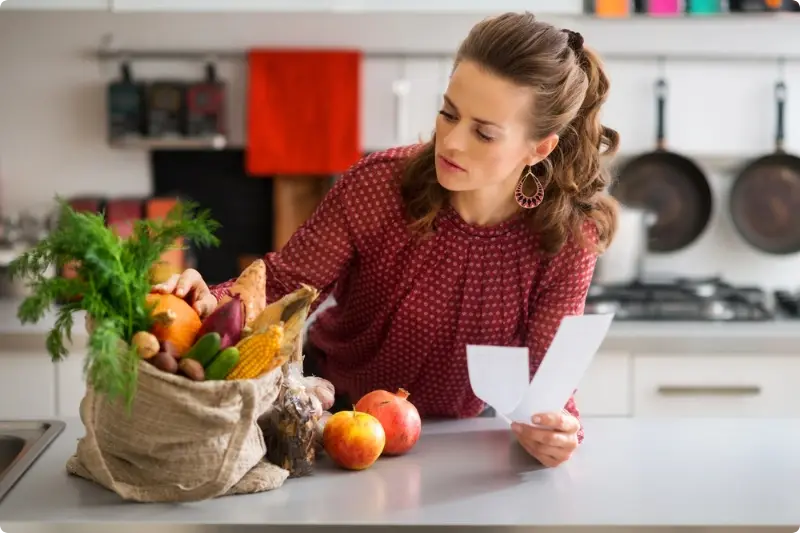 Vrouw met boodschappenlijstje in hand kijkend naar tas met groente