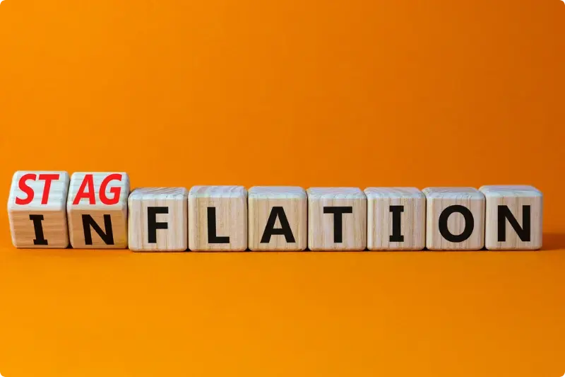 Houten blokjes die omvallen van 'inflation' naar 'stagflation', passend bij de vraag of stagflatie op de loer ligt