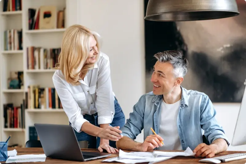 Man en vrouw achter een tafel met een laptop en brieven, lachend naar elkaar, passend bij tips om slim te beleggen