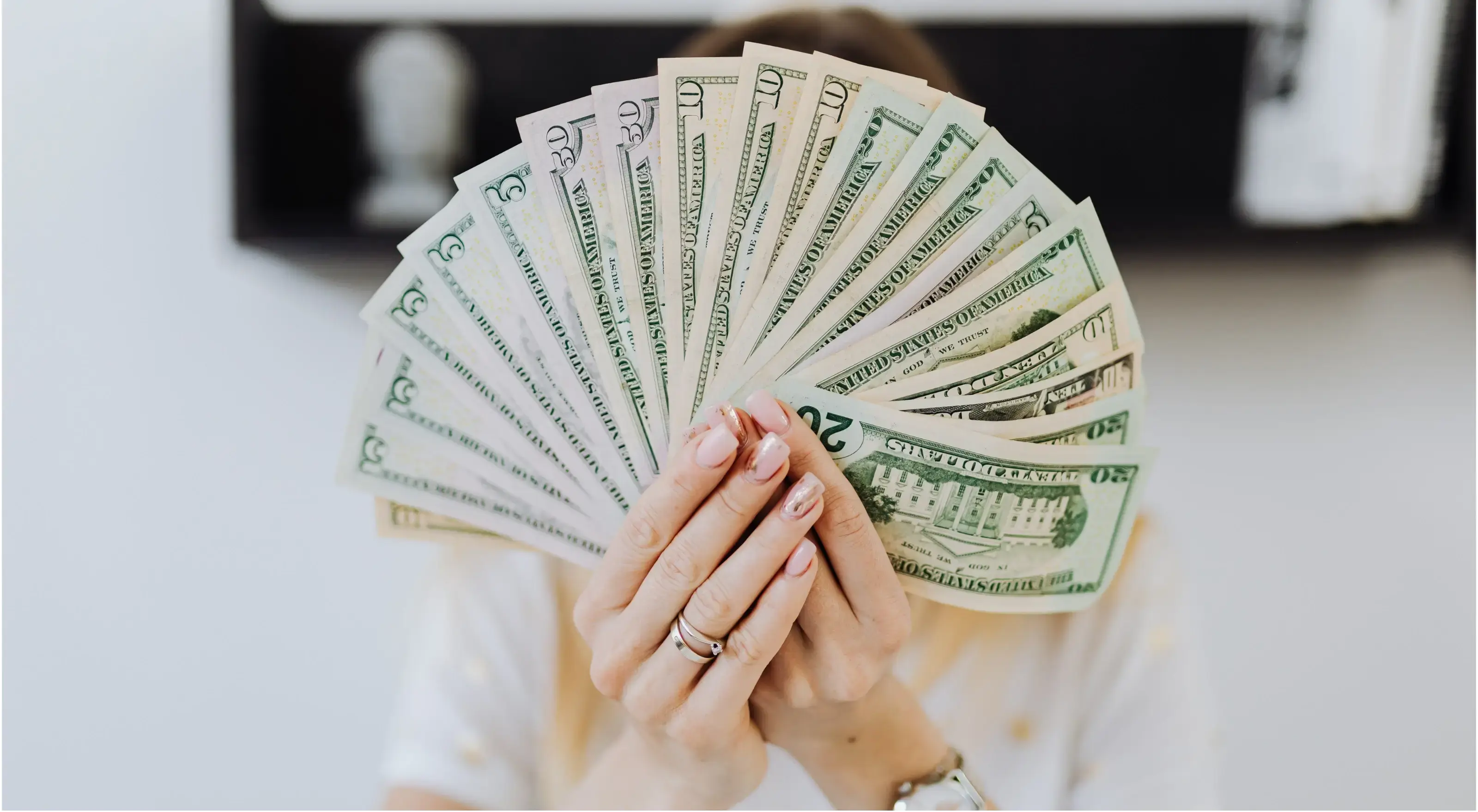 Afbeelding van een vrouw met allemaal briefjes van 20 dollar in haar hand. En dit verbergt haar gezicht.